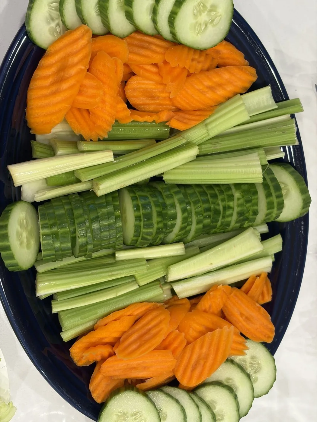 A symmetrical vegetable board with cucumber slices lined up in a neat row between celery sticks and carrot chips